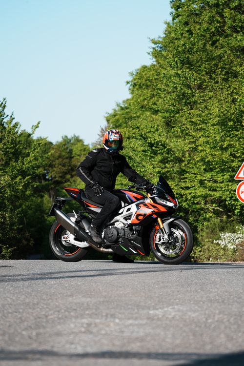 Free Motorcyclist in full gear riding a sport bike on a sunny day surrounded by greenery. Stock Photo