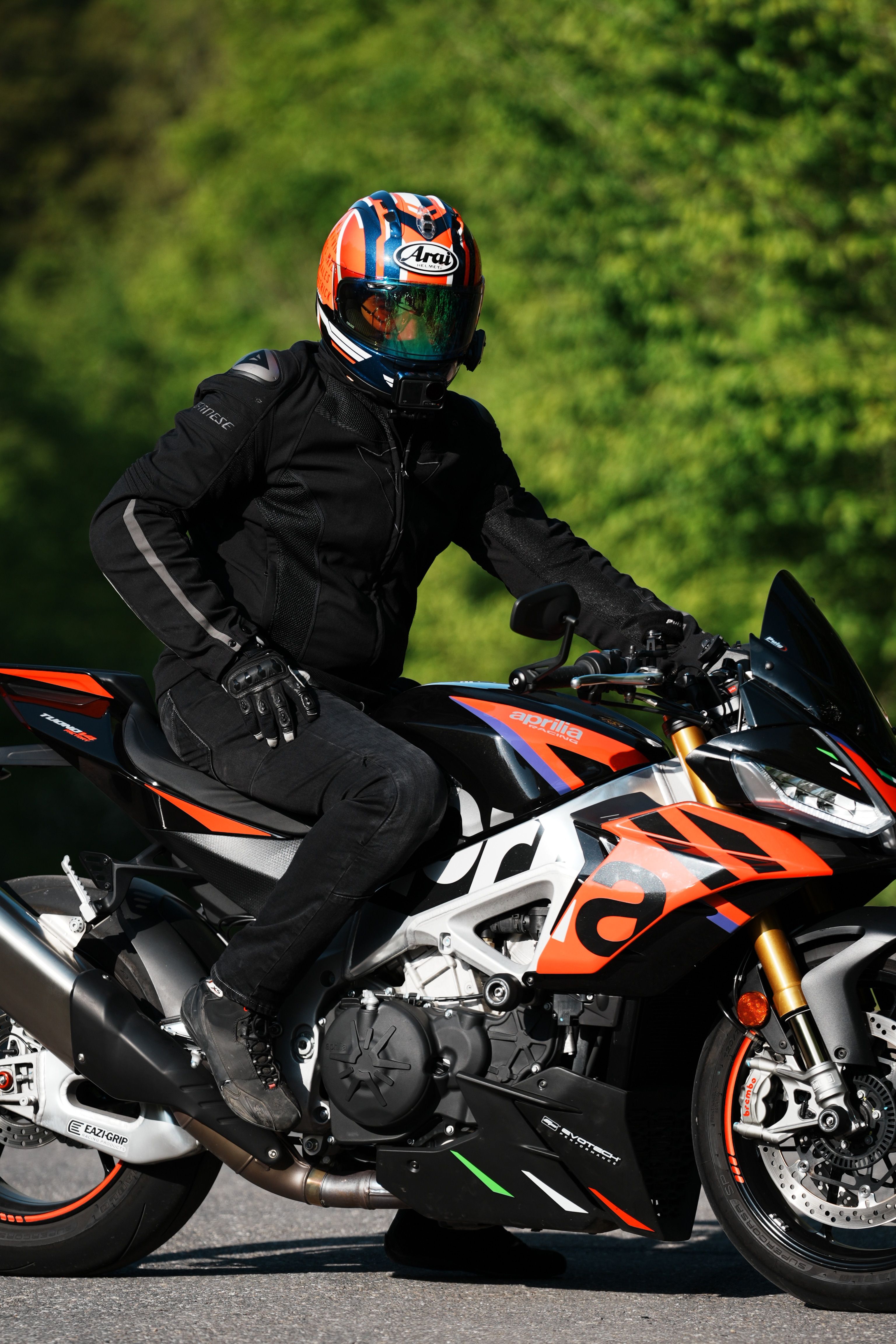 Motorcyclist in black gear riding a sport bike on a sunny road.