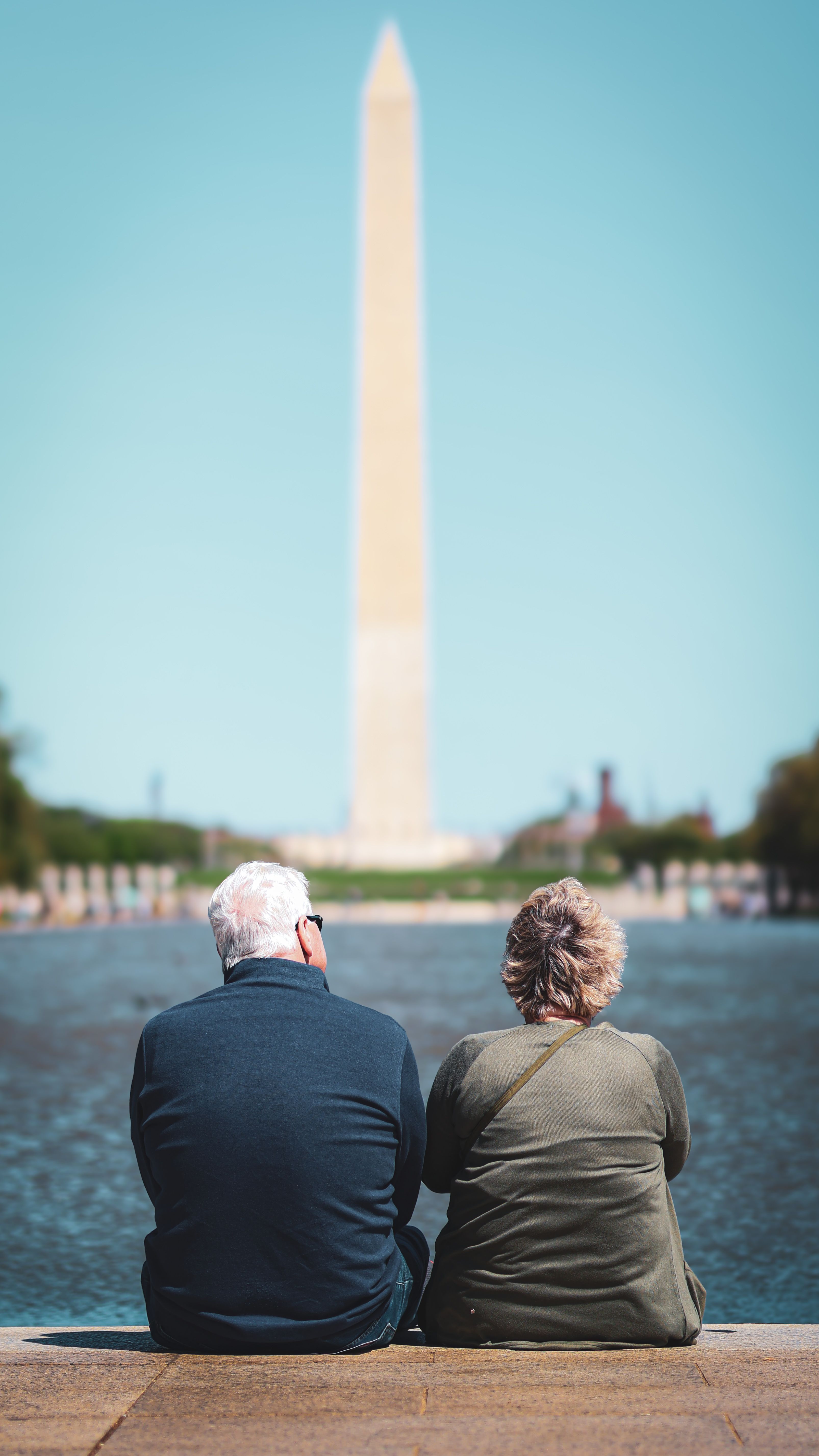 Elderly couple sitting by the reflecting pool with the Washington Monument in view. Captured in Washington, DC.