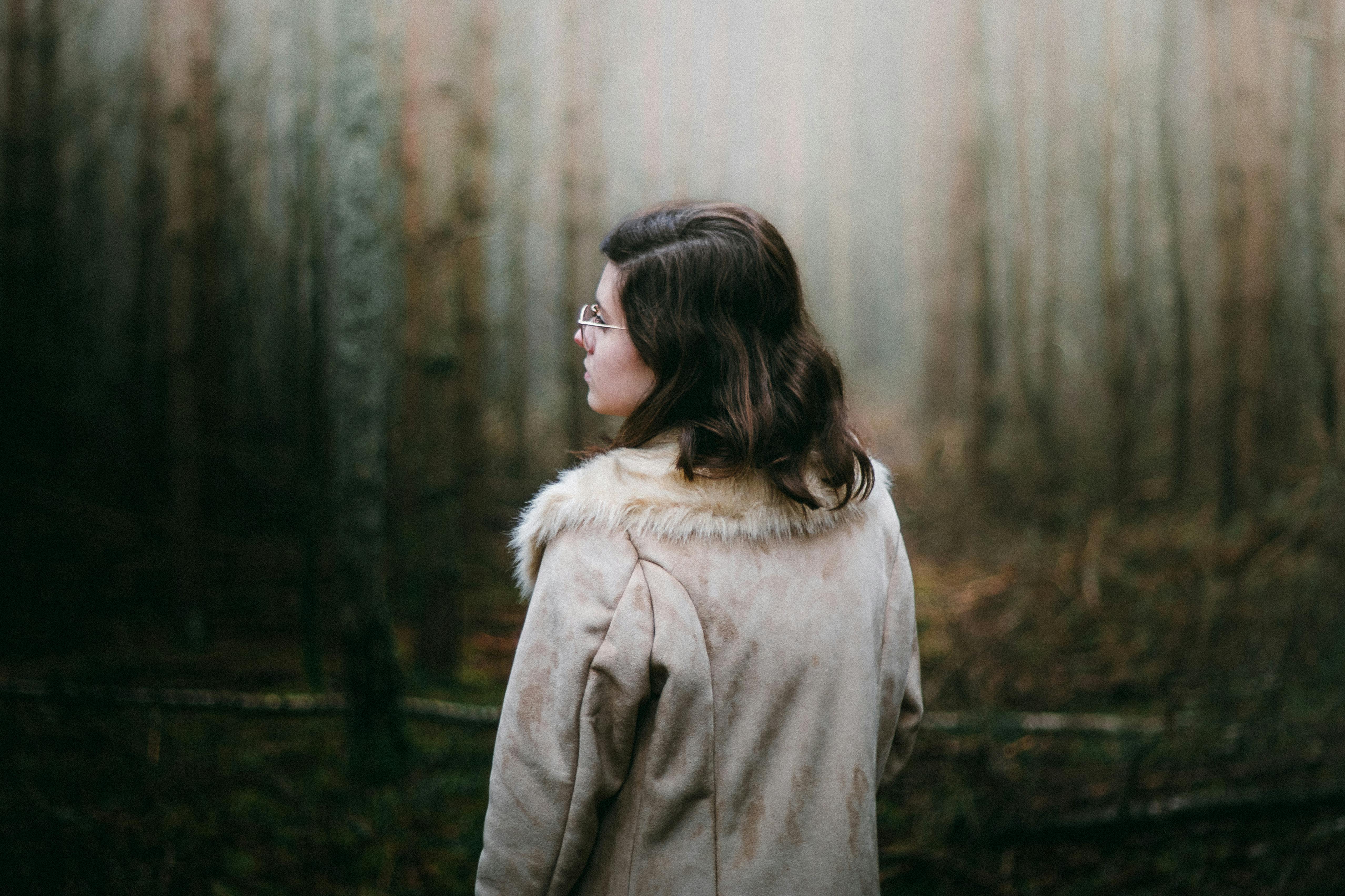 A woman in a fur coat gazes into a misty forest, evoking a sense of mystery and solitude.