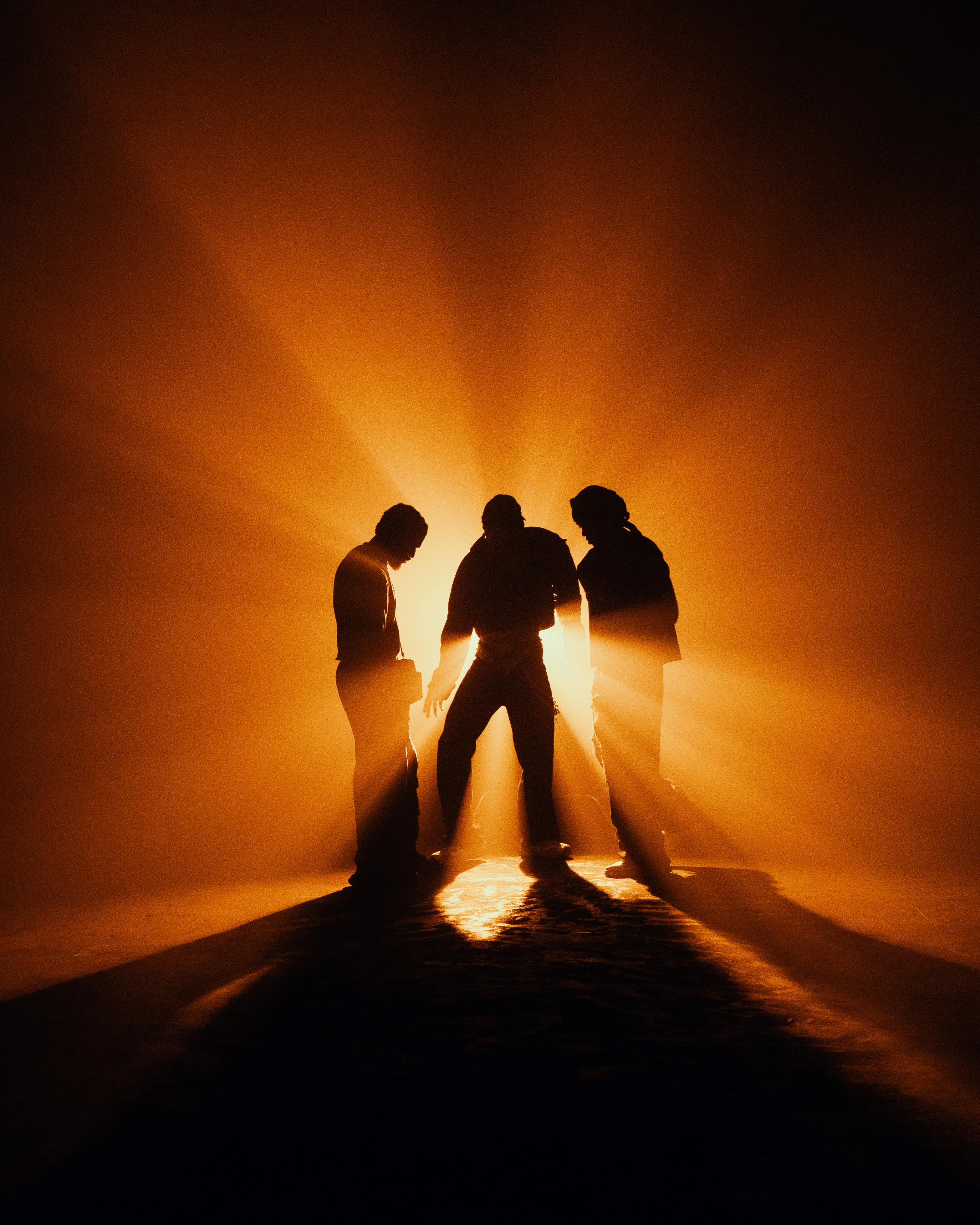 Three men silhouetted against dramatic orange lighting, creating a striking and mysterious scene.