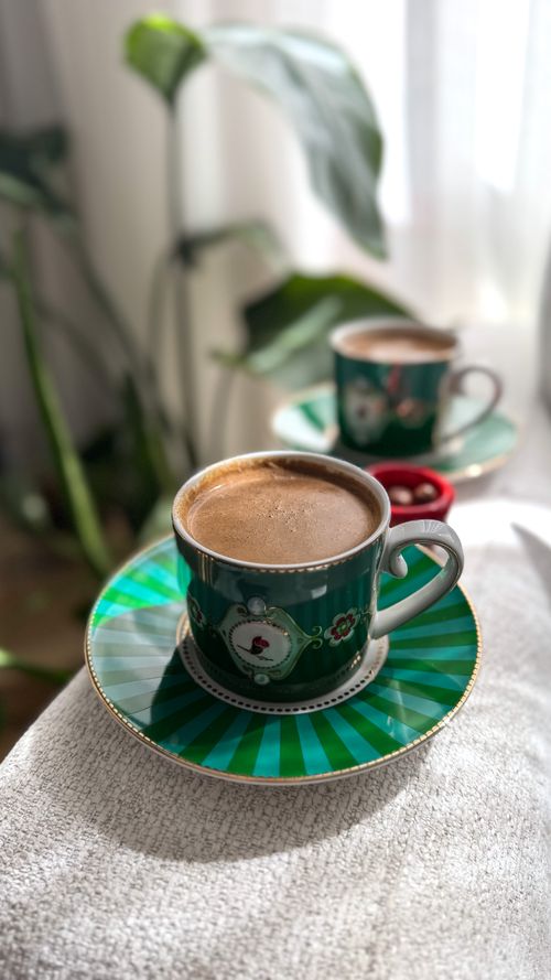Free Stylish green ceramic coffee cups on saucers with a cozy plant backdrop. Stock Photo