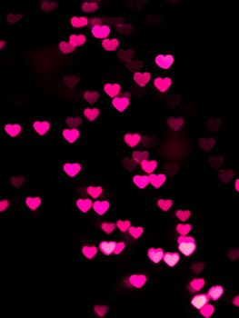 Vibrant pink heart-shaped bokeh lights create a romantic, dreamy atmosphere against a dark background.