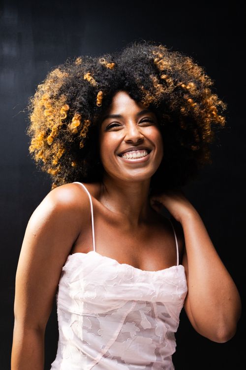 Free Portrait of a joyful woman with natural curly hair wearing a pink dress, captured in Sao Paulo, Brazil. Stock Photo