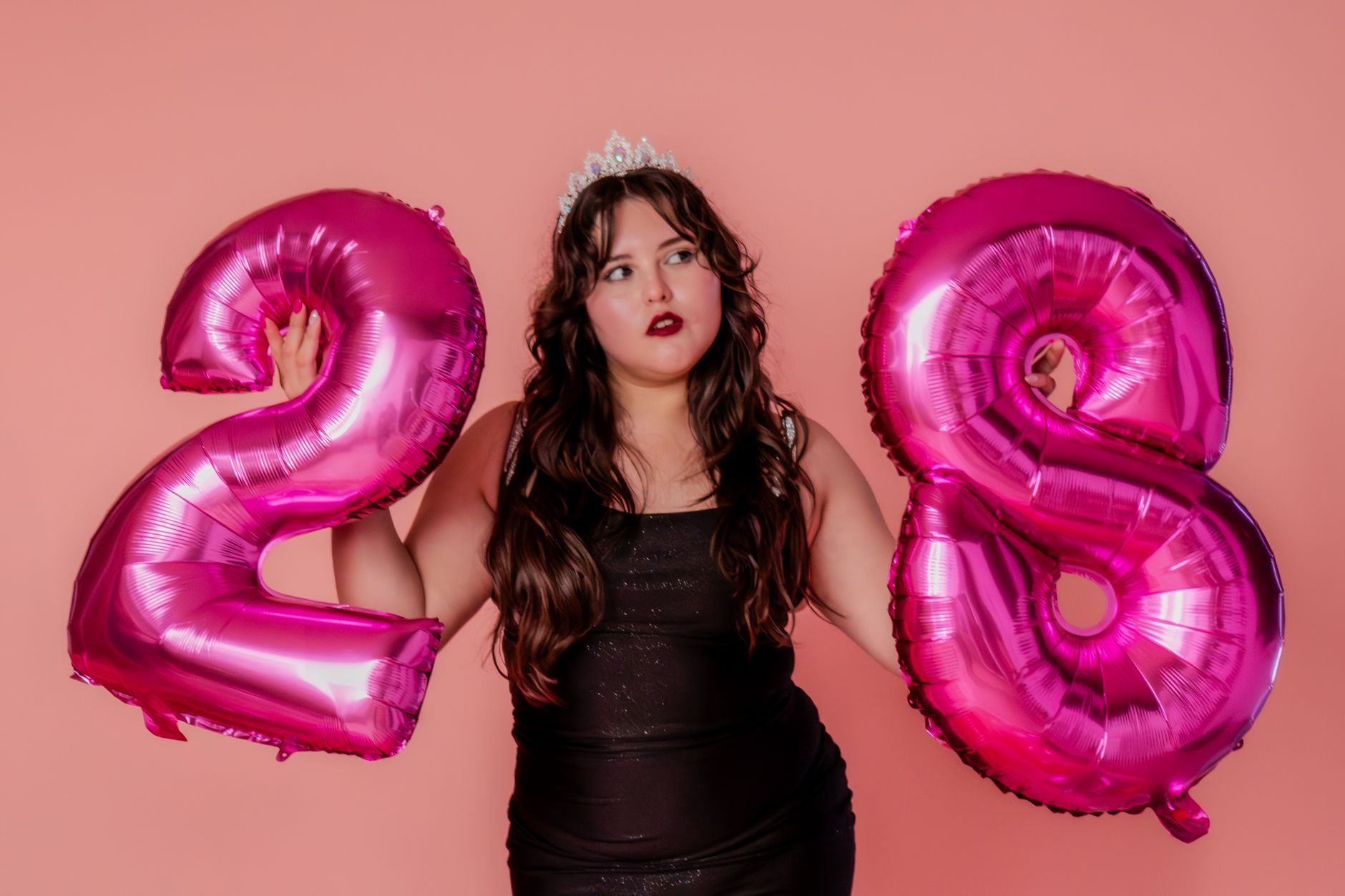 A woman holding pink number balloons against a vibrant backdrop.