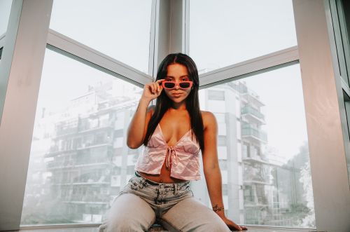 Free Young woman in pink top and sunglasses poses indoors with city view. Stock Photo