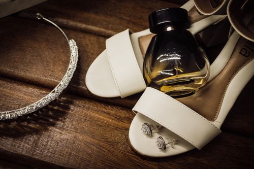 Free A stylish arrangement of bridal accessories including shoes, perfume, earrings, and a sparkling tiara on a wooden surface. Stock Photo