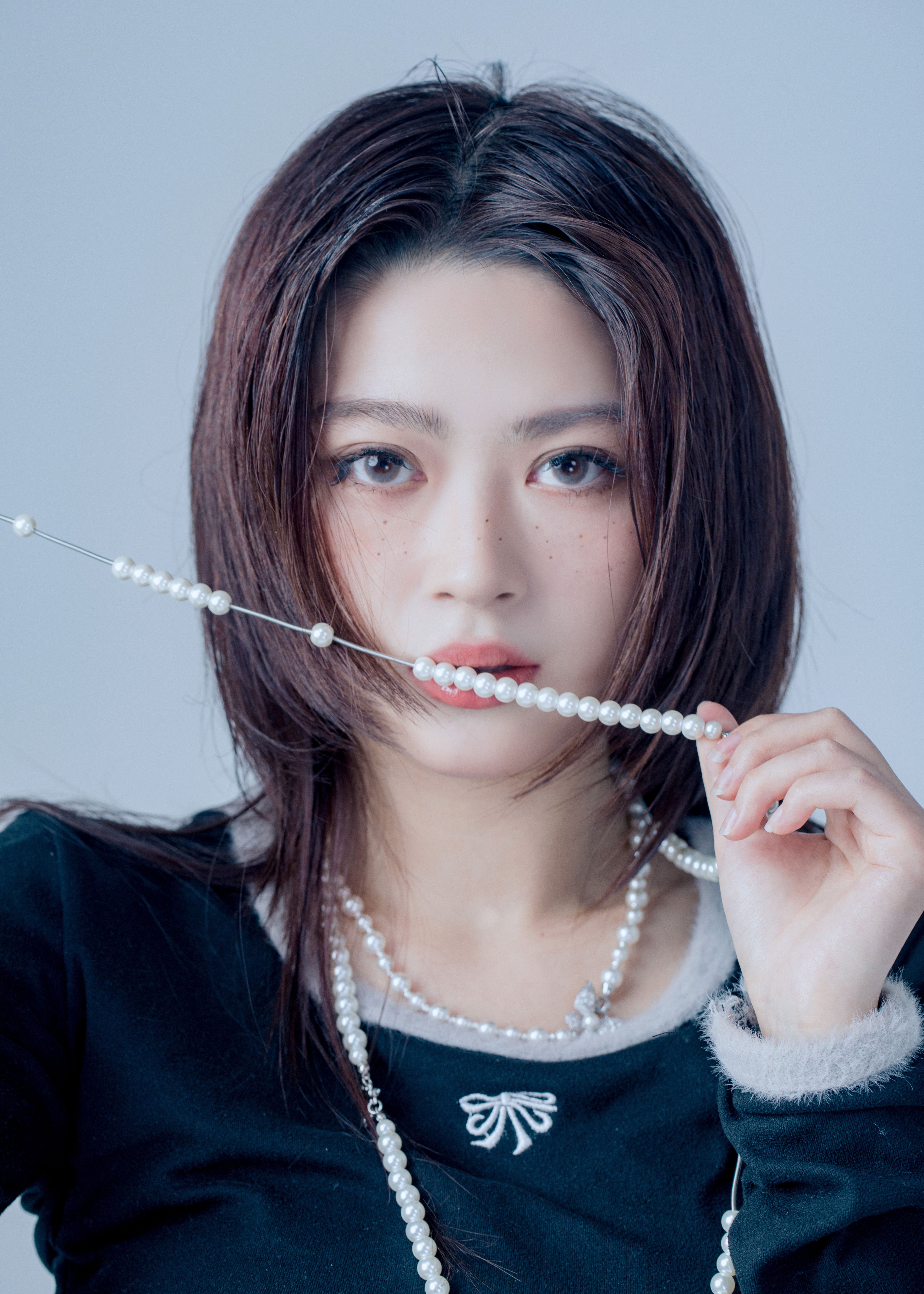 Striking portrait of a young woman holding a pearl necklace, expressing elegance and style.