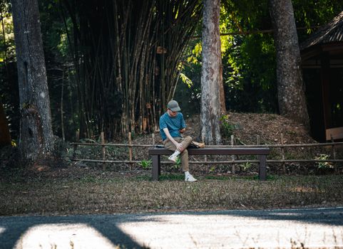 Casual moment captured of a person sitting on a bench in a tranquil Thai forest setting.