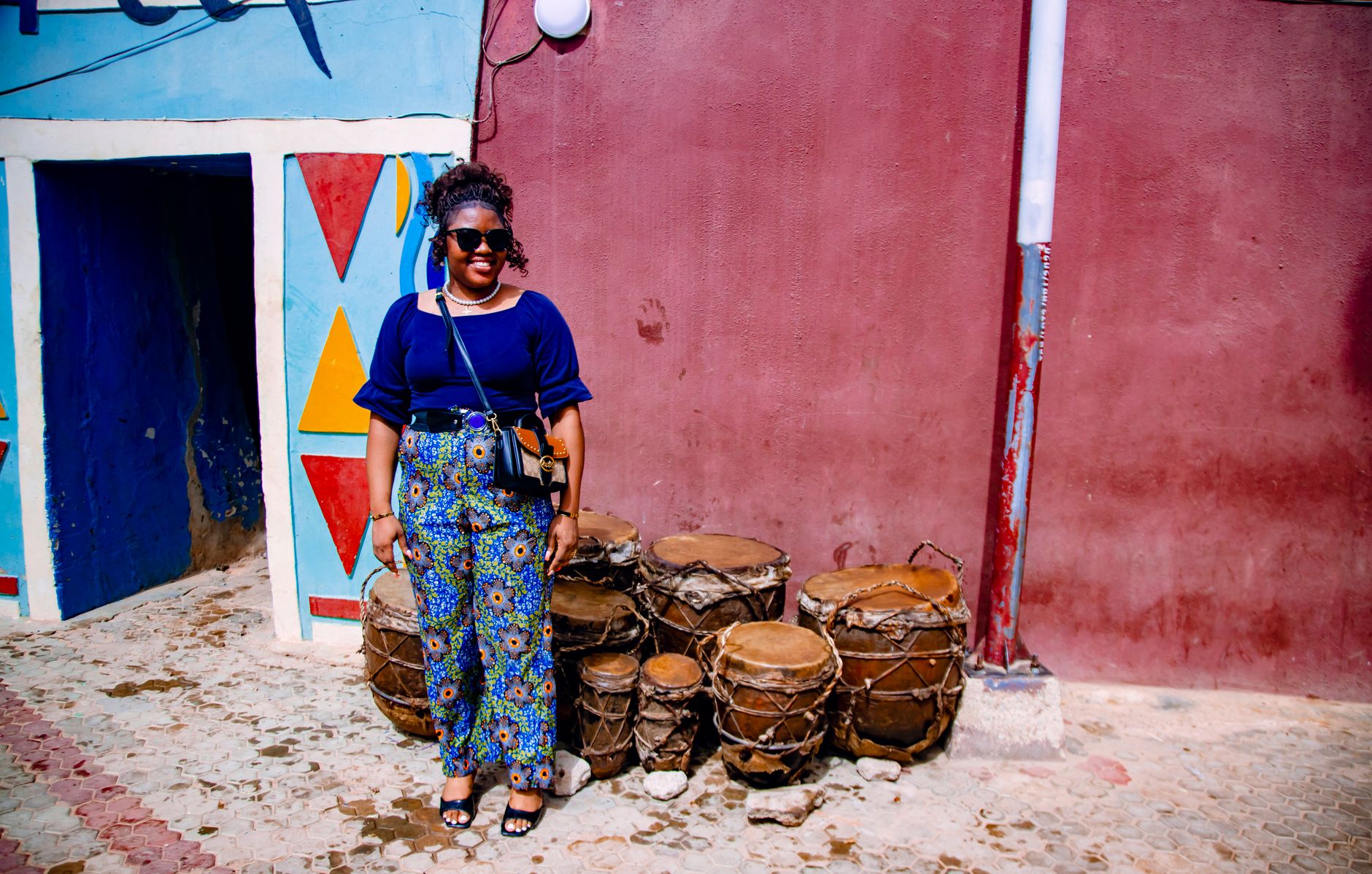 Smiling woman in sunglasses beside traditional drums and vibrant murals in Lagos