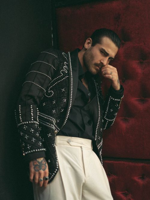 Free Fashionable man in a detailed jacket posing against a red velvet backdrop indoors. Stock Photo