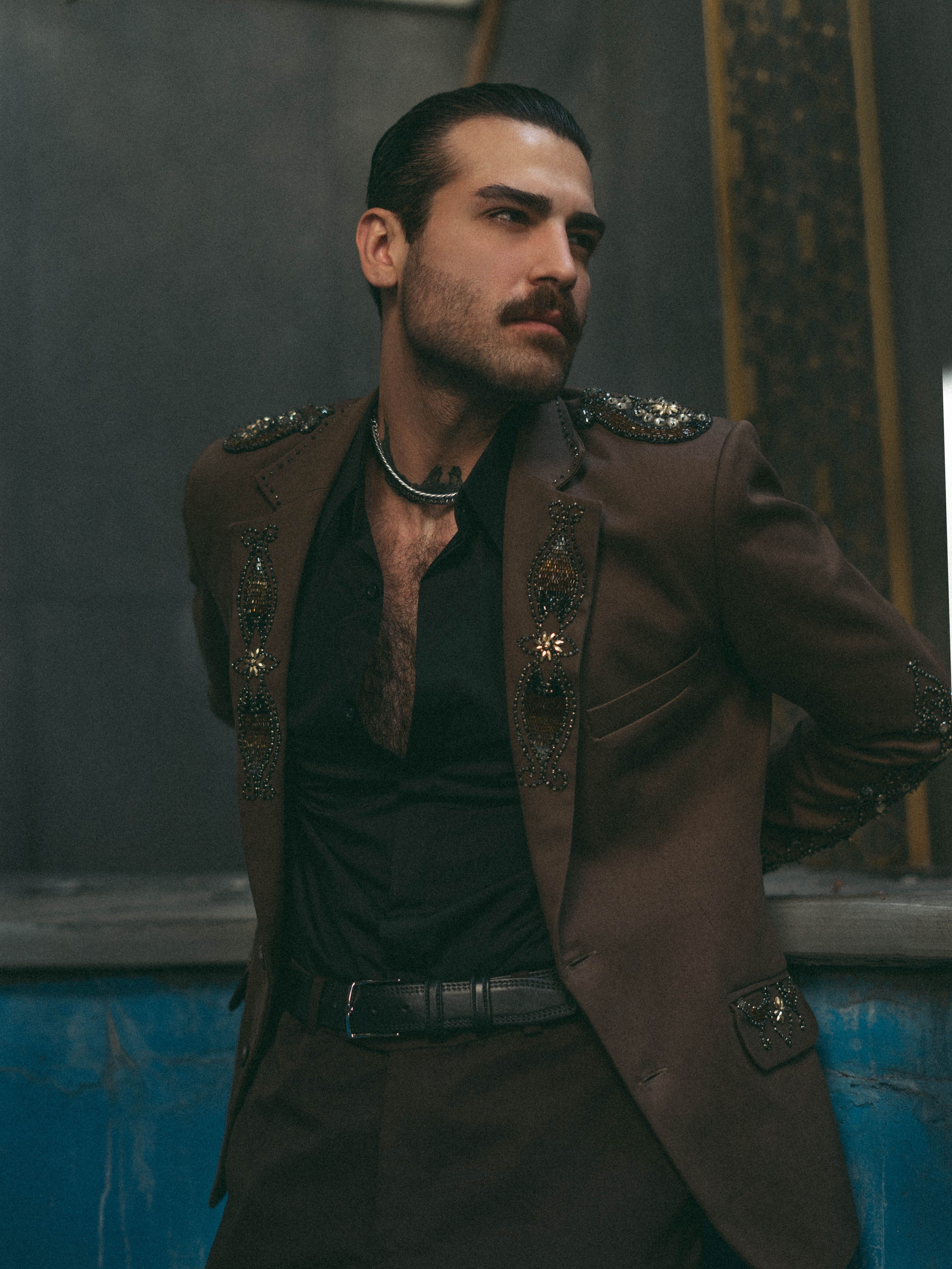 Sophisticated man in detailed suit posing confidently indoors.
