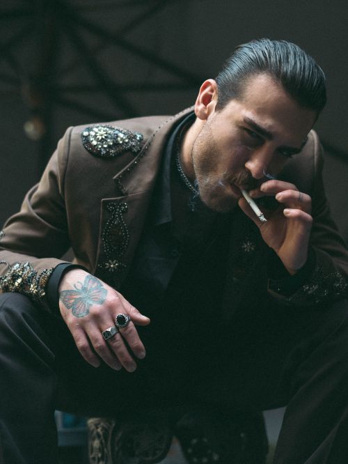 Free A man in a bejeweled jacket smokes indoors, exuding style and attitude. Stock Photo