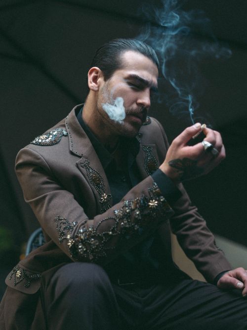 Free Portrait of a stylish man in a detailed suit smoking outdoors, exuding elegance and mystery. Stock Photo
