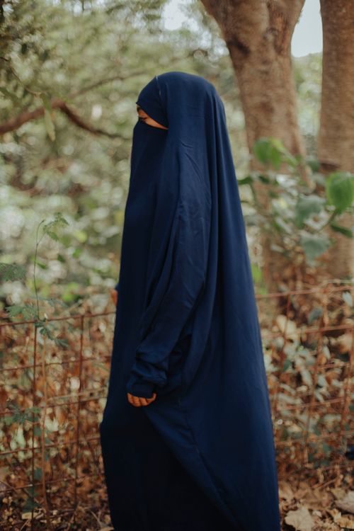 Free A woman in a blue niqab strolls through a serene forest setting, capturing natural beauty. Stock Photo