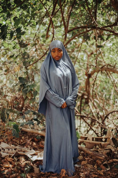 Free A young woman in a blue hijab standing confidently in a forest setting, surrounded by lush greenery. Stock Photo