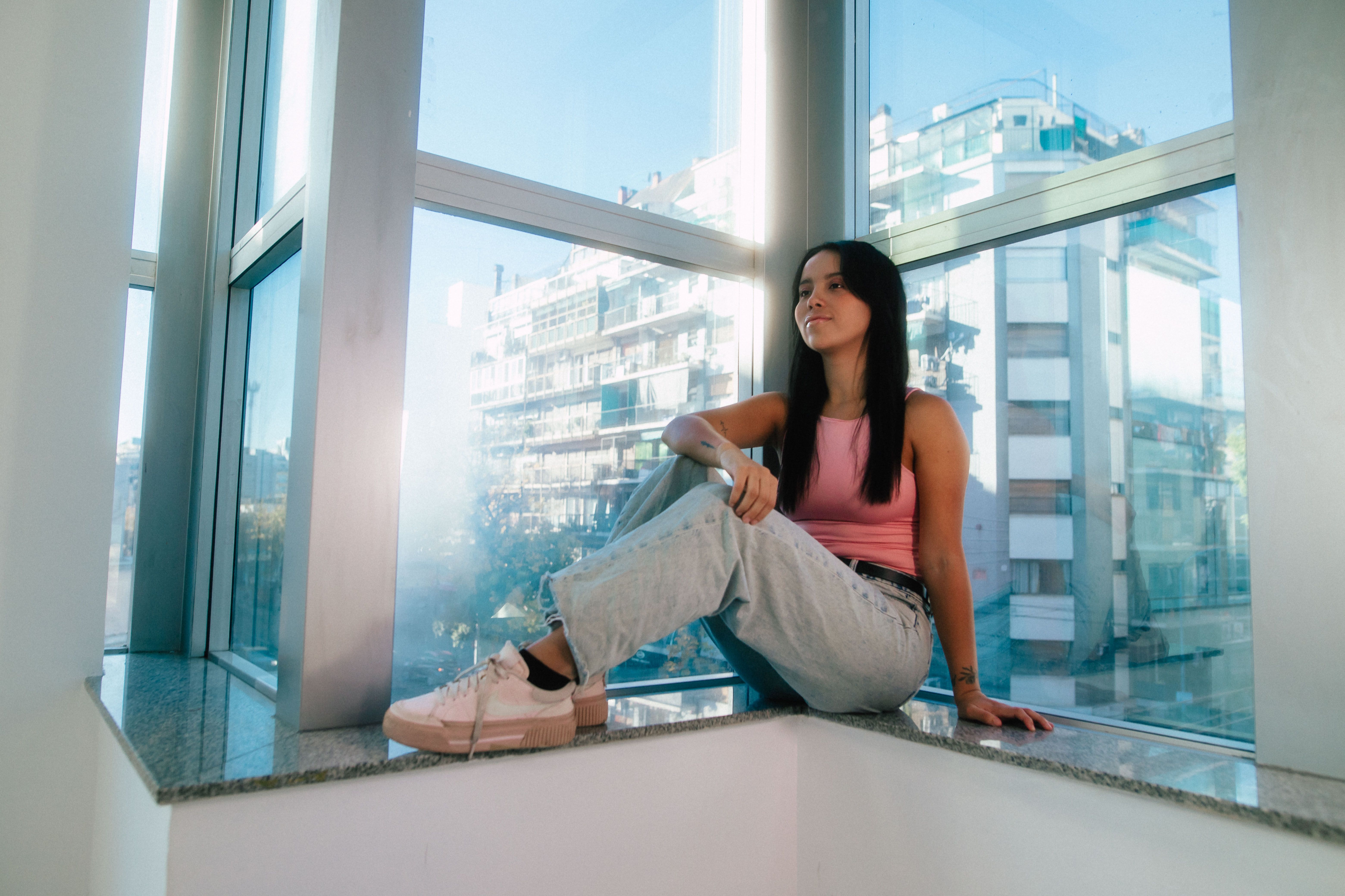 Relaxed young woman sitting by a window in Buenos Aires cityscape.
