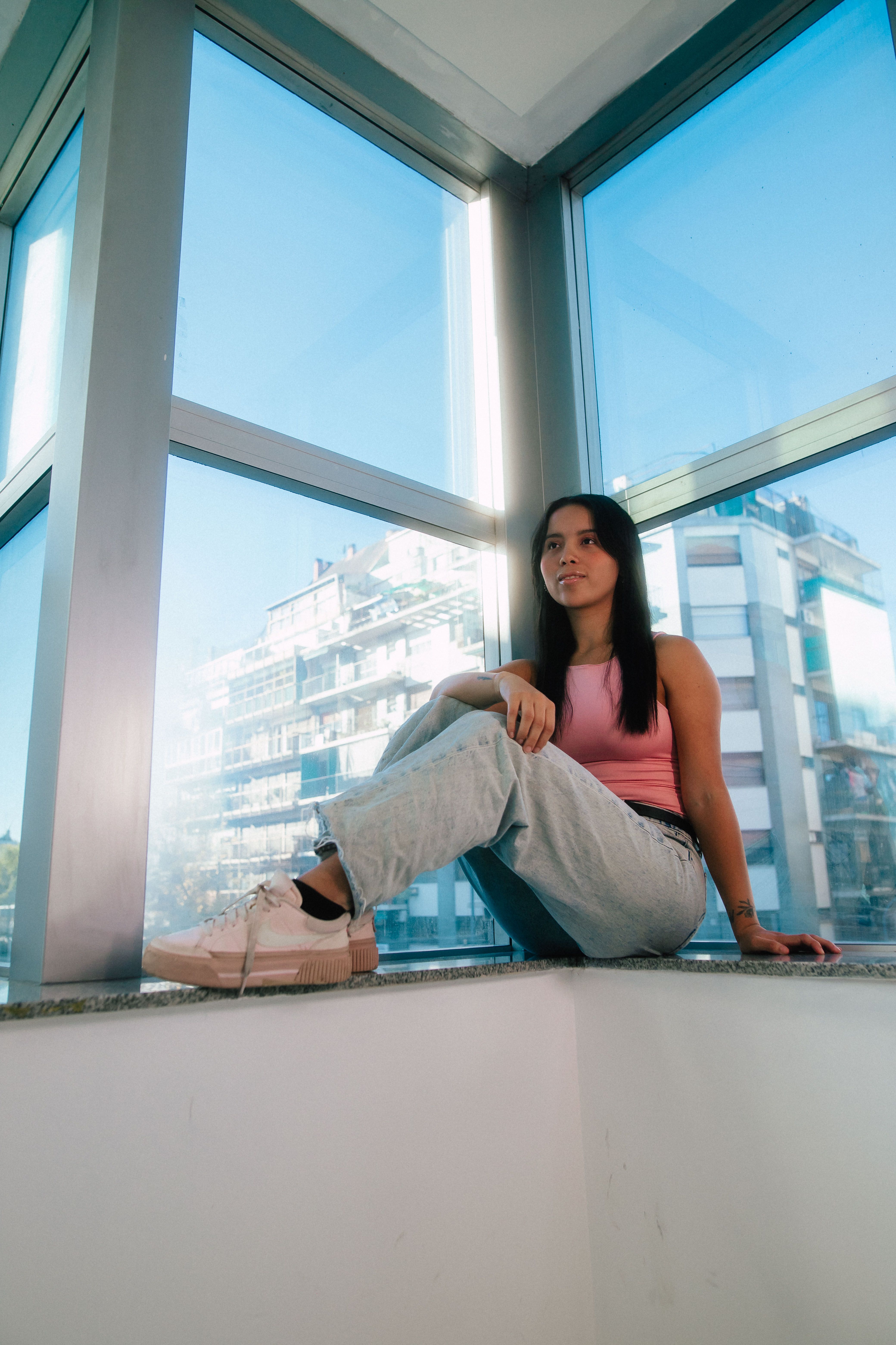 A young woman in casual attire sits by a large window with city views in Buenos Aires.