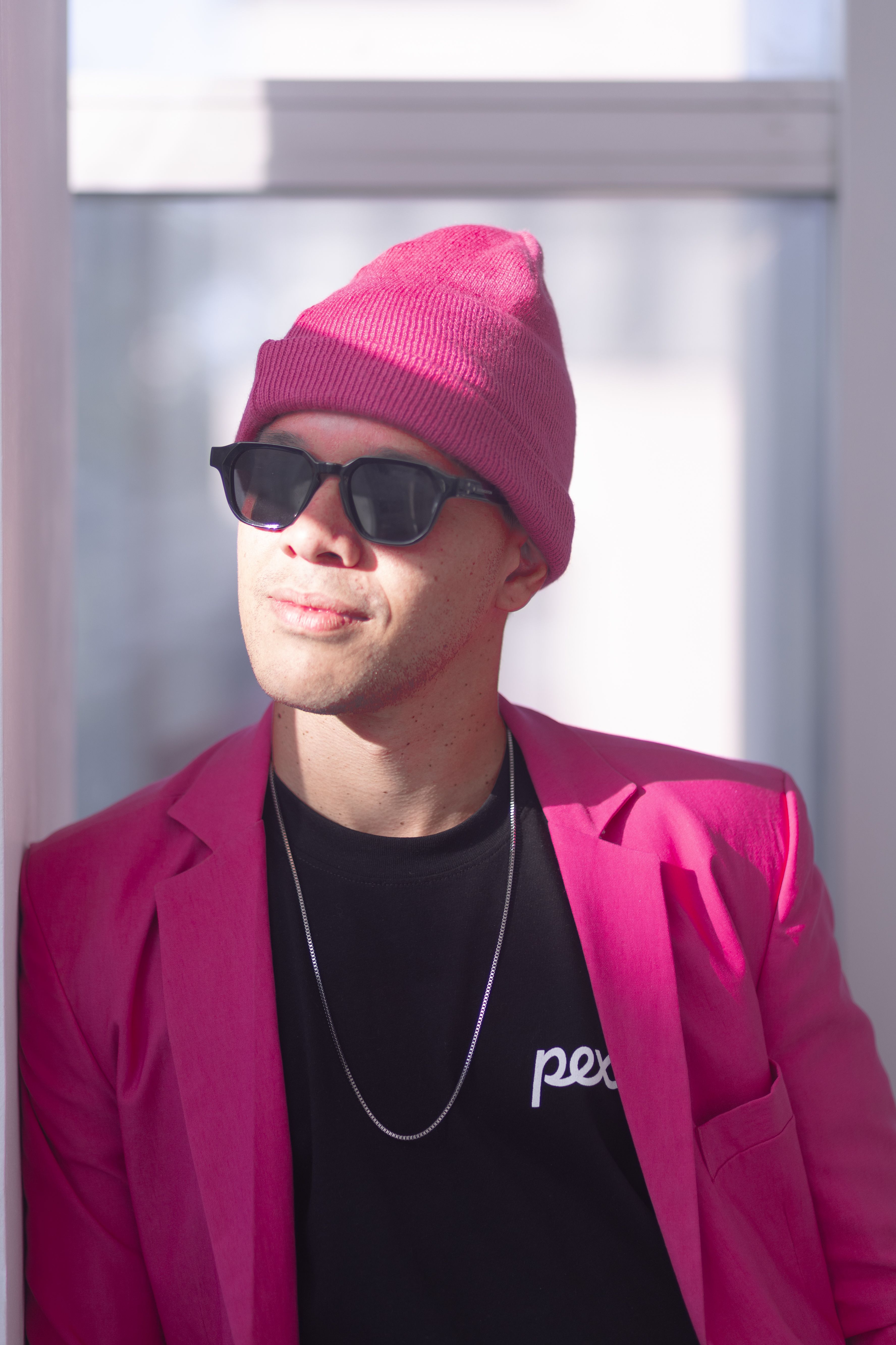 Portrait of a fashionable man wearing a pink beanie and blazer, exuding urban chic style.