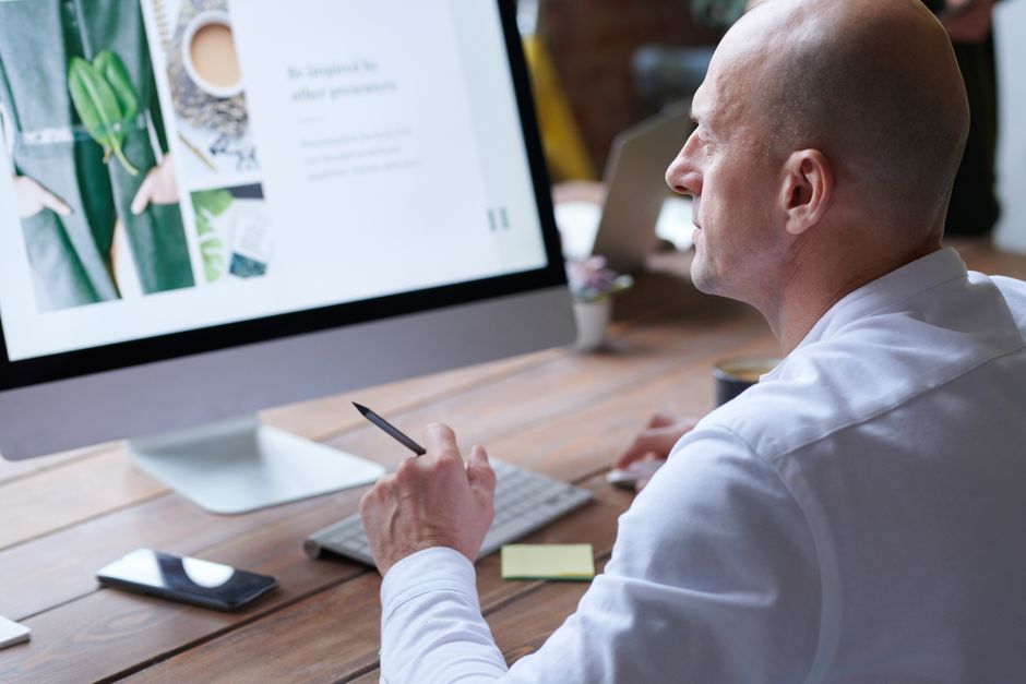 Homem careca se concentra no trabalho usando computador em escritório moderno. Design elegante e ferramentas digitais aumentam a produtividade.