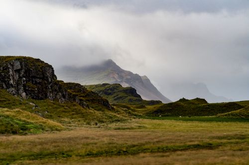 Free Captivating misty mountain landscape with grassy hills and rocky formations under a cloudy sky. Stock Photo