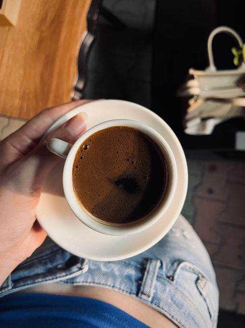Free Hand holding a cup of coffee over blue denim and wooden surface indoors. Stock Photo