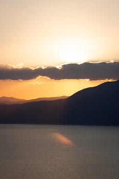 Breathtaking view of a sunset over mountains and a calm lake, capturing nature's tranquil beauty.