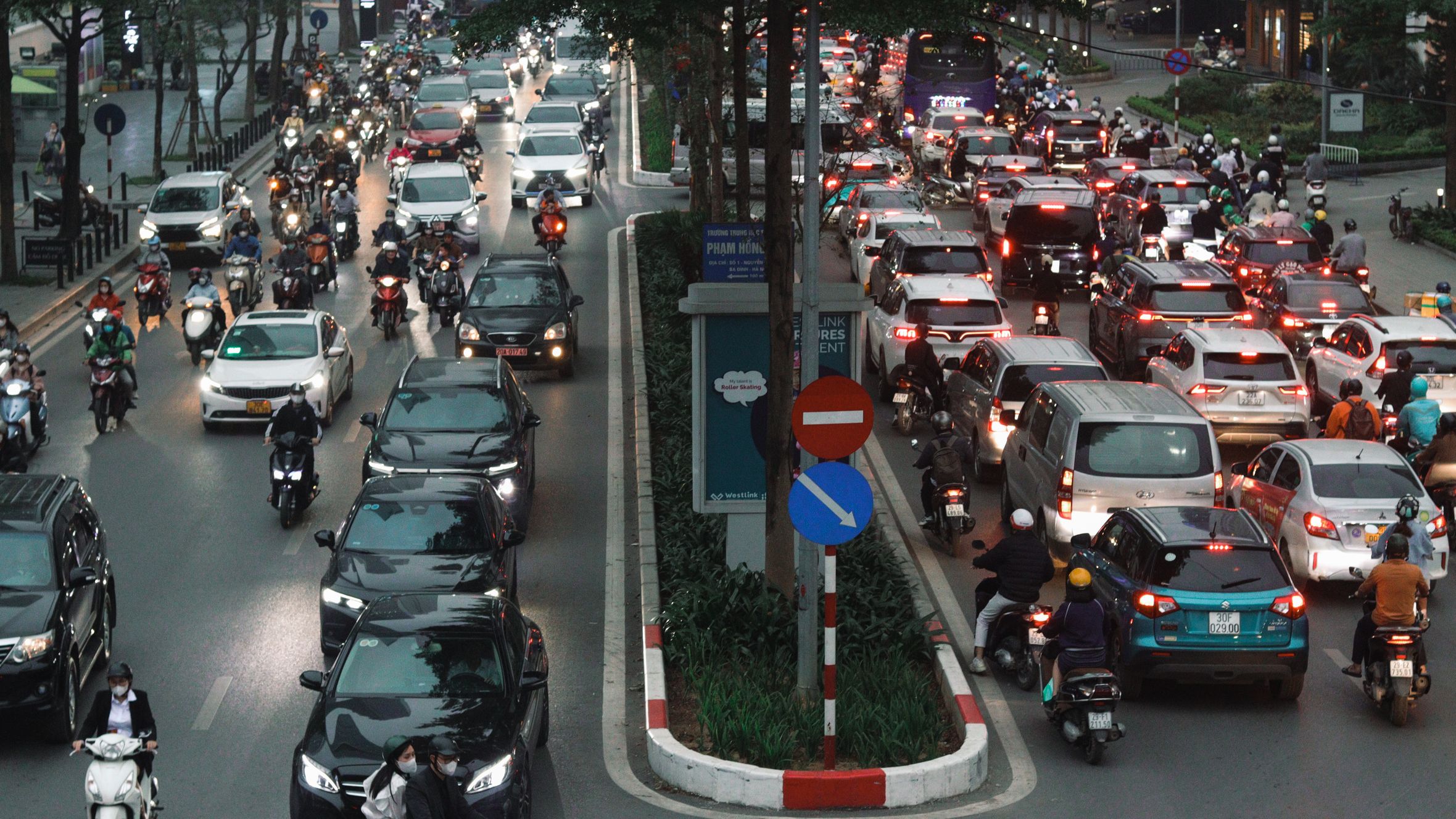 Busy city street packed with cars and motorcycles during evening rush hour.
