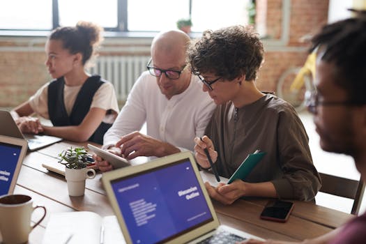 A group of adults working together on laptops and tablets in a modern office setting.