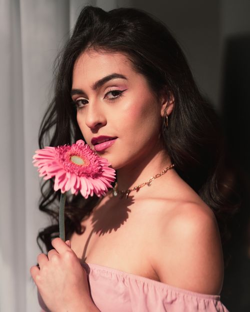 Free Stylish woman holding a pink gerbera daisy, sunlight casting soft shadows indoors. Stock Photo