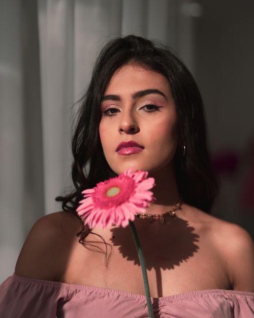 Free A portrait of a stylish woman holding a pink gerbera, showcasing elegance and beauty. Stock Photo