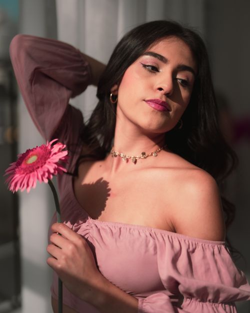 Free A captivating indoor portrait of a woman holding a pink flower, exuding elegance and charm. Stock Photo
