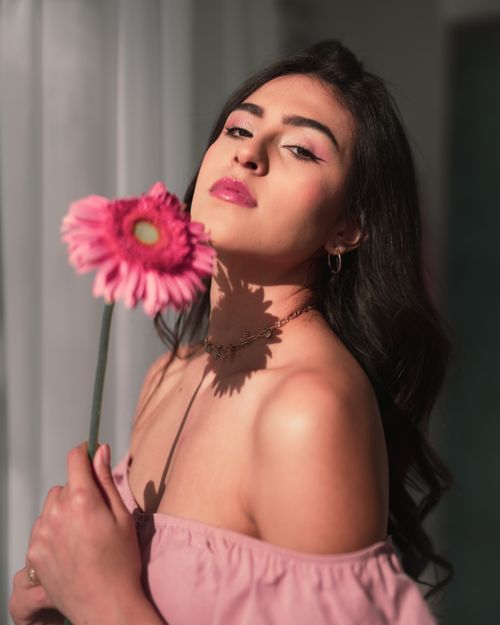 Free Elegant woman in soft light holding a pink flower, exuding charm and beauty. Stock Photo