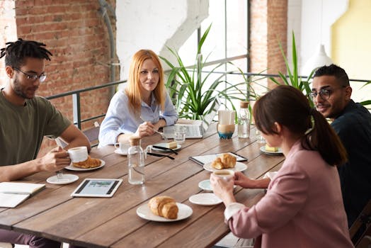 Team of diverse adults having a collaborative meeting with coffee and pastries in a modern office setting.
