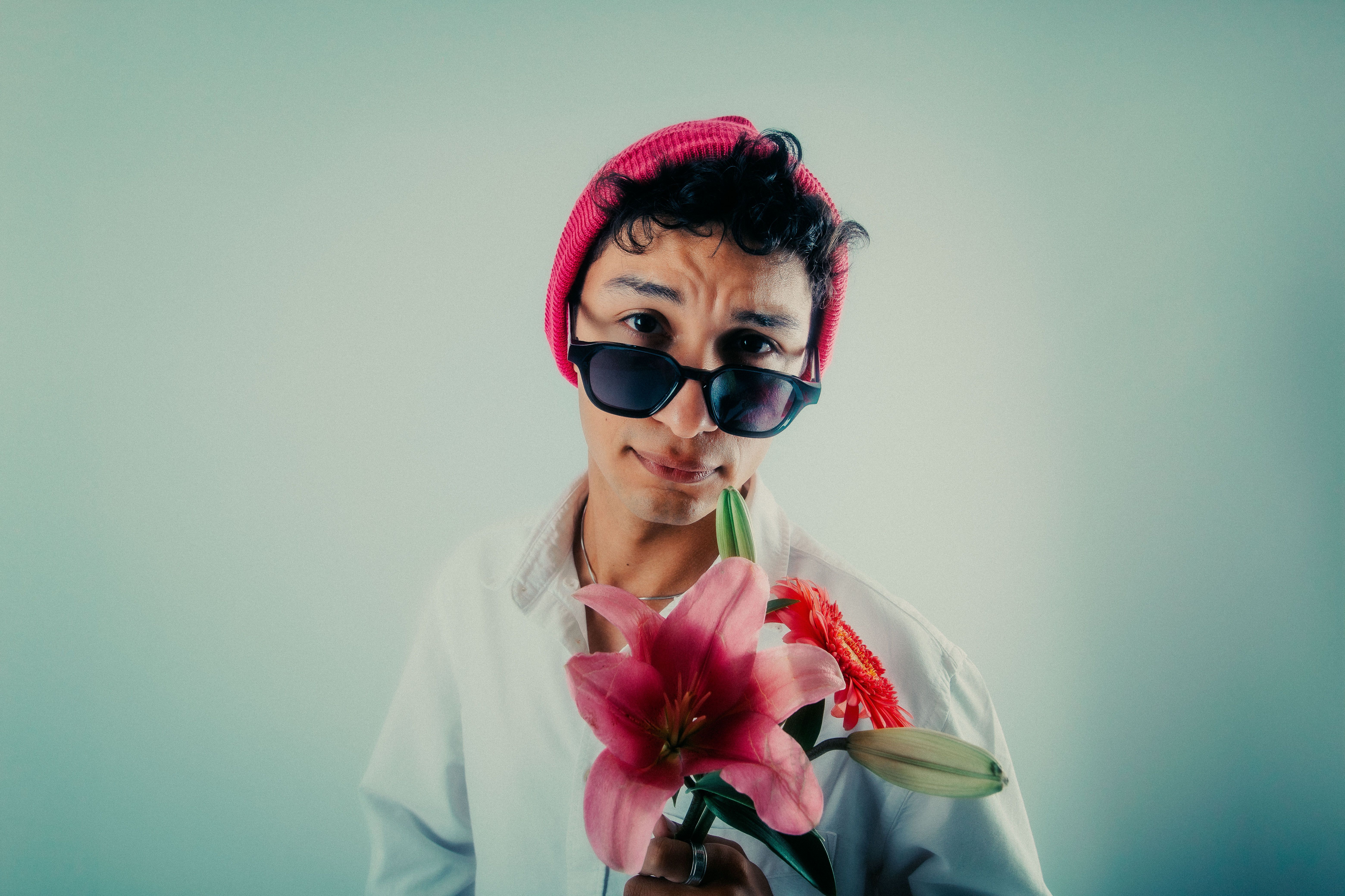 Young man wearing pink hat and sunglasses, holding flowers, indoors in Buenos Aires.