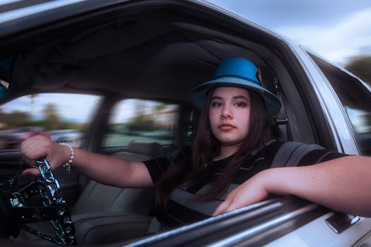 A young woman wearing a blue hat is seated in a classic car, exuding a calm and confident demeanor.