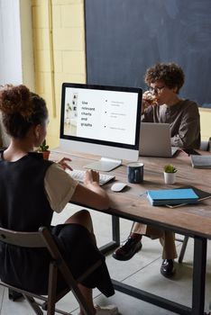 Two adults in an office discussing data on a computer screen.