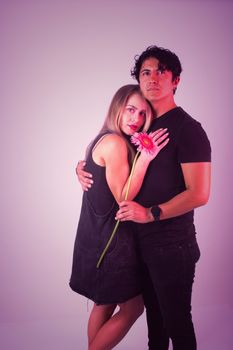 Young couple embracing with a pink gerbera flower in a modern studio portrait.