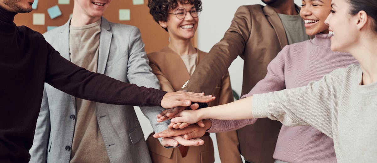 Team von Mitarbeitenden legt motiviert die Hände zusammen – Symbol für Zusammenhalt, Teamwork und erfolgreiche digitale Transformation im Mittelstand