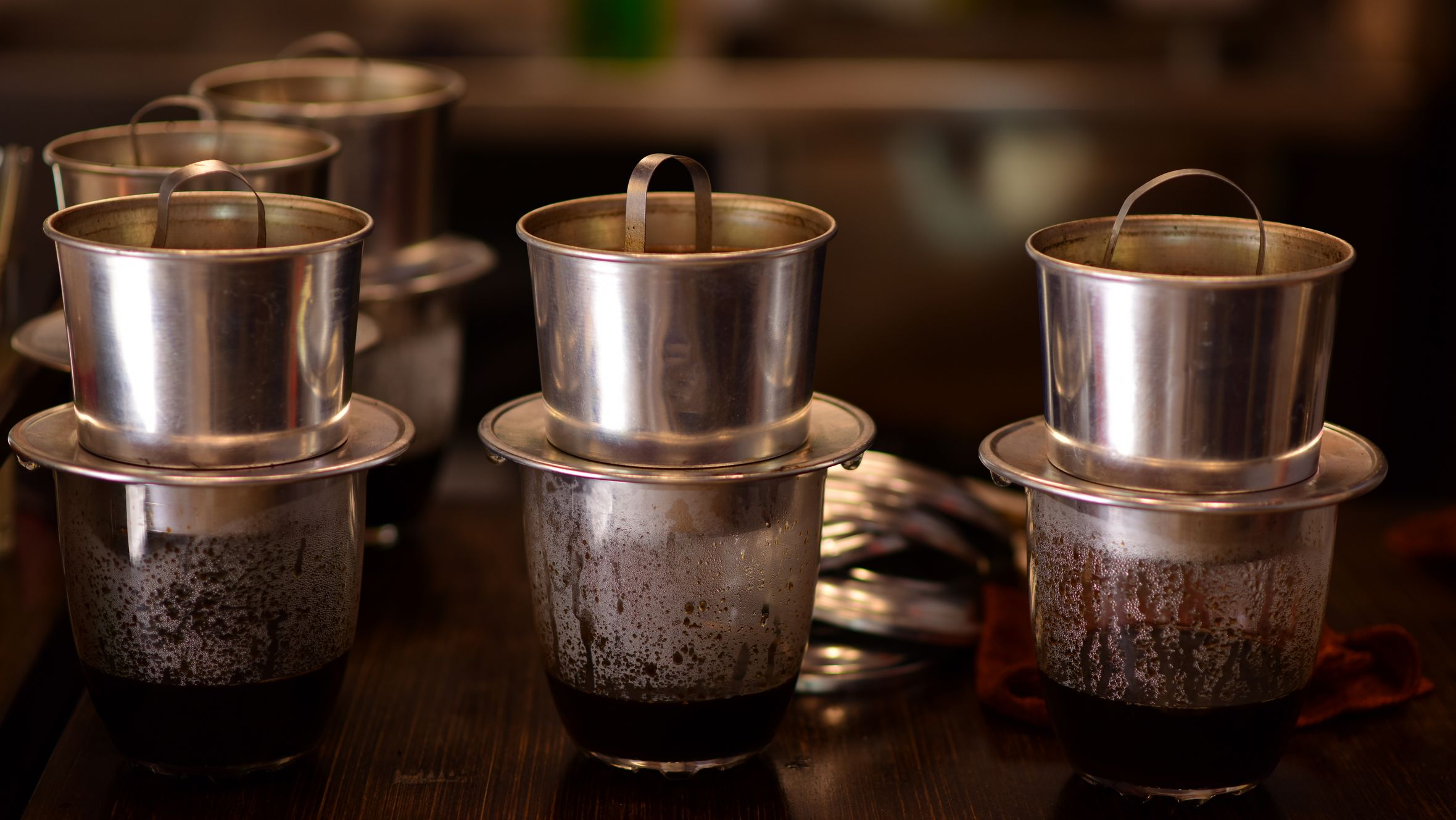 Close-up of Vietnamese drip coffee makers on a dark wooden table indoors.