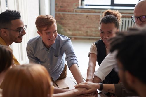 Free A diverse group of young professionals joining hands in a cheerful and supportive team-building activity. Stock Photo