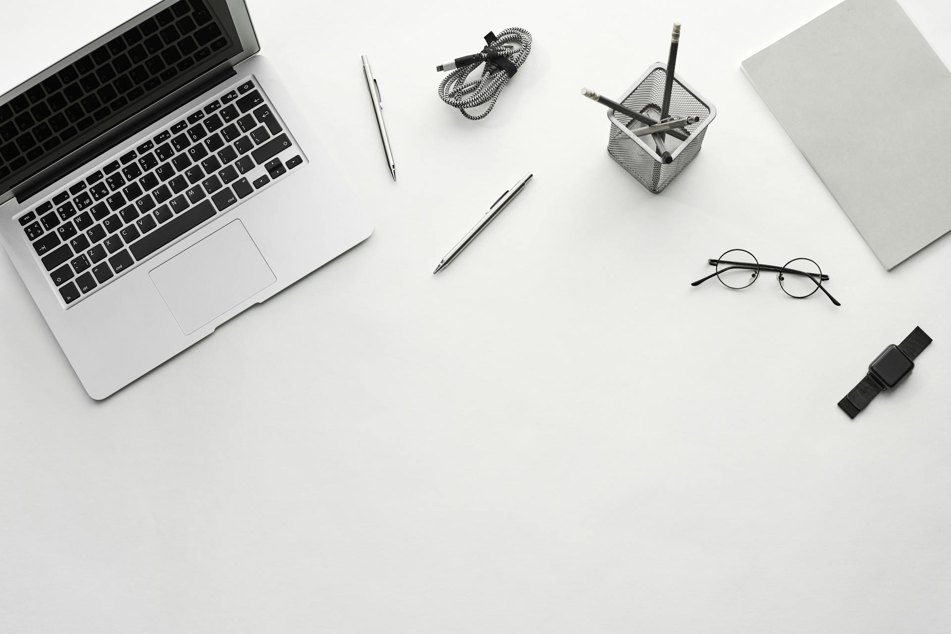 Top view of a minimalist workspace featuring a laptop, glasses, and office supplies on a white desk.