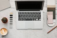 从时尚工作空间的顶视图看去，大理石桌面上摆放着笔记本电脑、拿铁咖啡、仙人掌和彩色样本