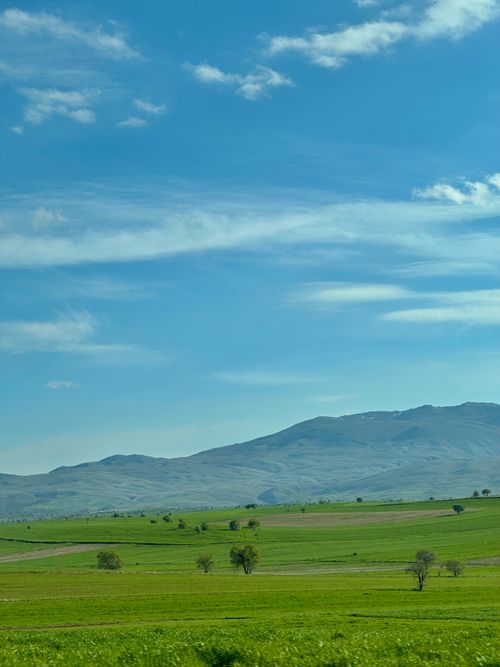 Free Expansive green fields with distant hills beneath a bright blue sky and clouds. Stock Photo