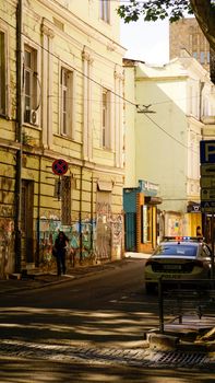 A city street featuring old buildings, graffiti, and a parked police car in bright daylight.