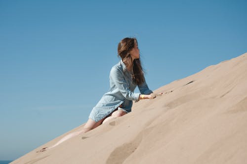 Женщина в синей рубашке с длинным рукавом сидит на коричневом песке
