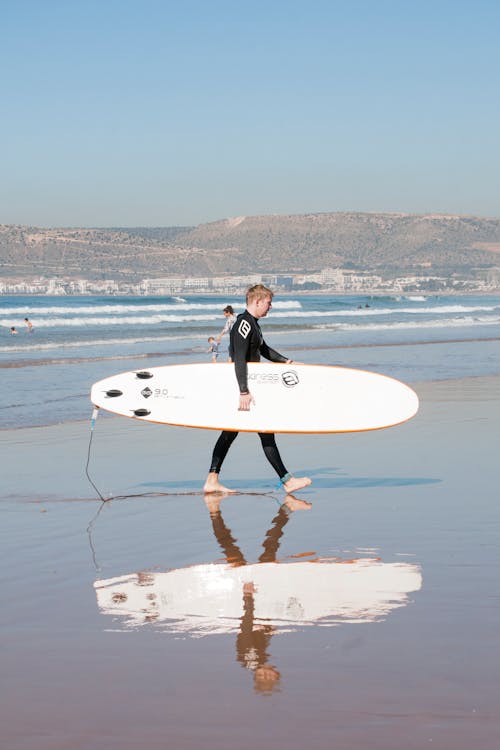 Woman in Black Wet Suit Carrying
 White Surfboard on Beach