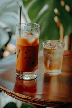Two refreshing iced drinks on a wooden table with a leafy background.