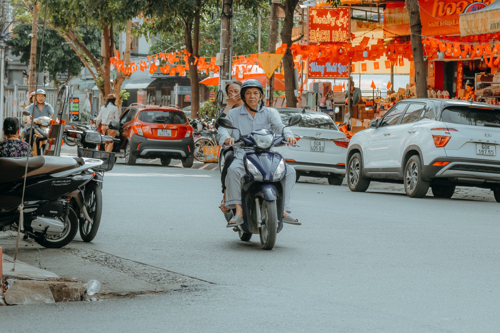 Bustling street market scene with motorbike riders wearing helmets amidst colorful stalls.