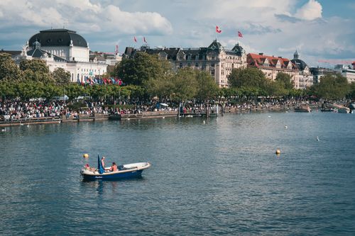 Free Scenic view of a boat on Lake Zurich with Zurich city buildings and Swiss flags. Stock Photo
